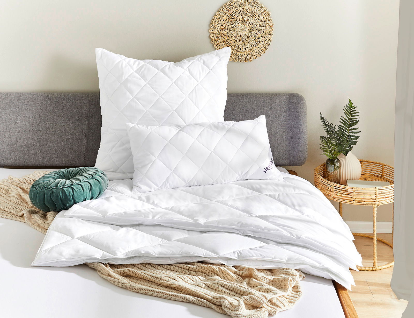 Bett mit weißen Kopfkissen und Bettdecke, dekoriert mit einem grünen Kissen und einem Strickplaid, seitliche Perspektive