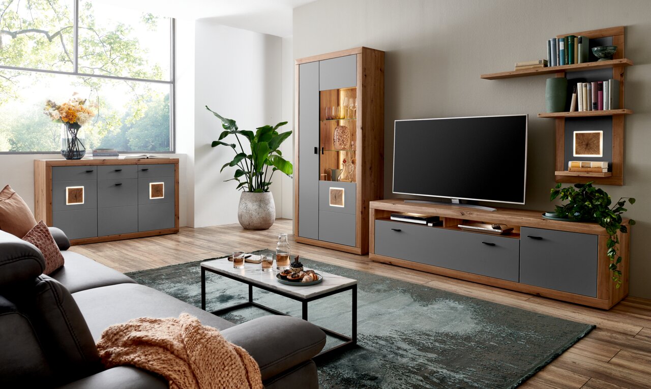 Moderne Wohnzimmer-Wandkombination in Holzoptik mit grauen Fronten, bestehend aus TV-Board, Vitrine und Regal, seitliche Perspektive.