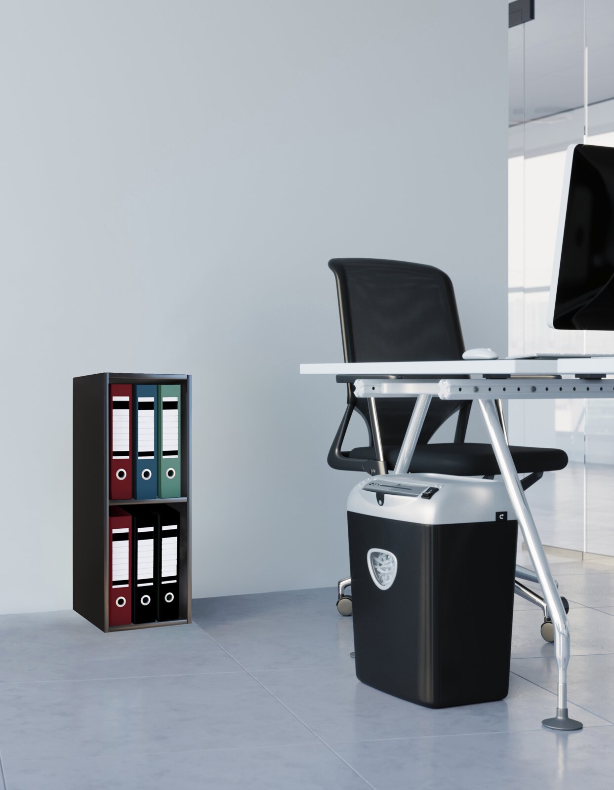 Moderner Aktenvernichter in Schwarz-Silber unter einem Büroschreibtisch neben einem kleinen Ordnerregal, seitliche Perspektive auf Bodenhöhe