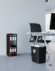 Moderner Aktenvernichter in Schwarz-Silber unter einem Büroschreibtisch neben einem kleinen Ordnerregal, seitliche Perspektive auf Bodenhöhe