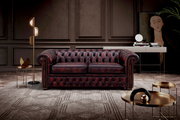 Elegantes, dunkelrotes Chesterfield-Sofa mit zwei Sitzplätzen in einem stilvoll eingerichteten Wohnzimmer, frontal betrachtet.