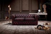 Elegantes, dunkelrotes Chesterfield-Sofa mit zwei Sitzplätzen in einem stilvoll eingerichteten Wohnzimmer, frontal betrachtet.