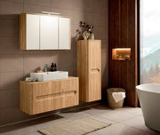 Modernes Badezimmer-Set in heller Holzoptik mit wandhängendem Waschtischunterschrank und Aufsatzwaschbecken, Hochschrank sowie Spiegelschrank mit LED-Leuchte, frontal in leichter Schrägansicht von links fotografiert.