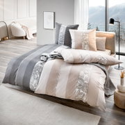 Modernes Bett mit Bettwäsche-Set in Beige, Weiß und Grau mit Streifen- und Paisley-Muster, dekorativen Kissen und Tagesdecke in hellem Schlafzimmer mit großer Fensterfront und Bergblick, Perspektive: schräg von vorne (3/4-Ansicht)