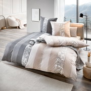 Modernes Bett mit Bettwäsche-Set in Beige, Weiß und Grau mit Streifen- und Paisley-Muster, dekorativen Kissen und Tagesdecke in hellem Schlafzimmer mit großer Fensterfront und Bergblick, Perspektive: schräg von vorne (3/4-Ansicht)