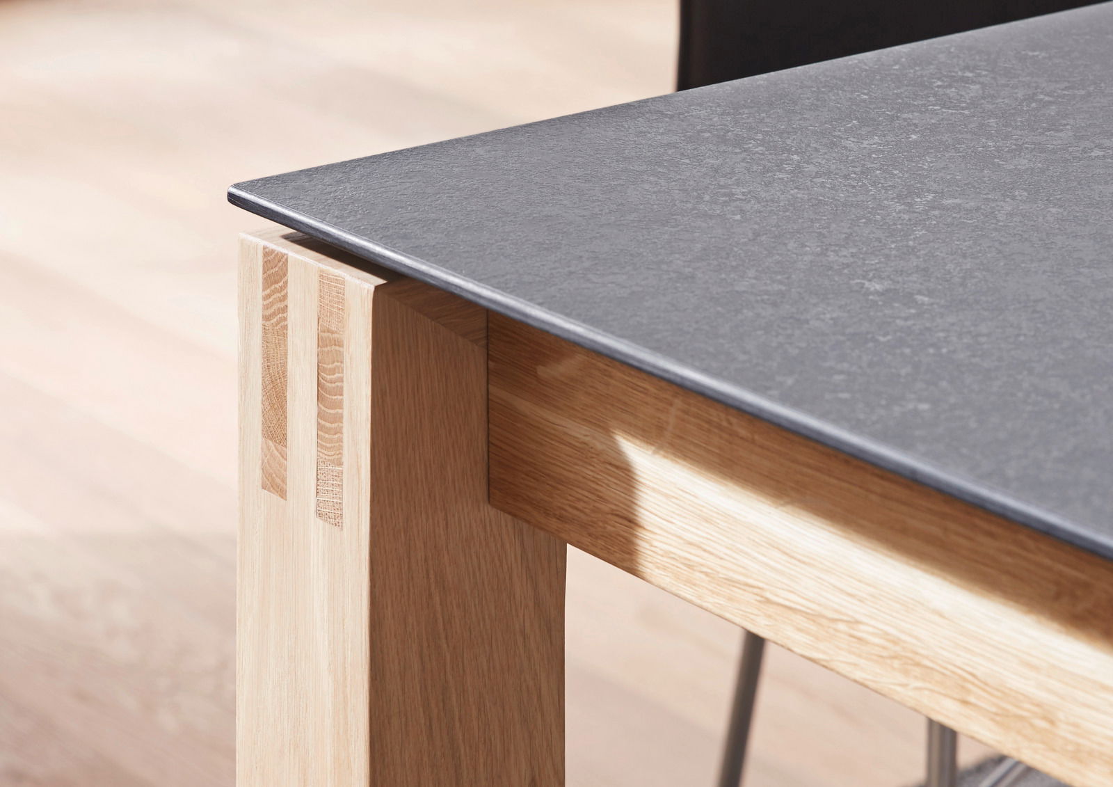 Nahaufnahme eines Esstisches mit einer dunklen Tischplatte und einem hellen Holzgestell, seitliche Perspektive.