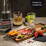 Eiswürfelform mit roten Beeren, präsentiert auf einem Holztablett mit Longdrink-Glas, Früchten und Gewürzen, seitliche Perspektive.