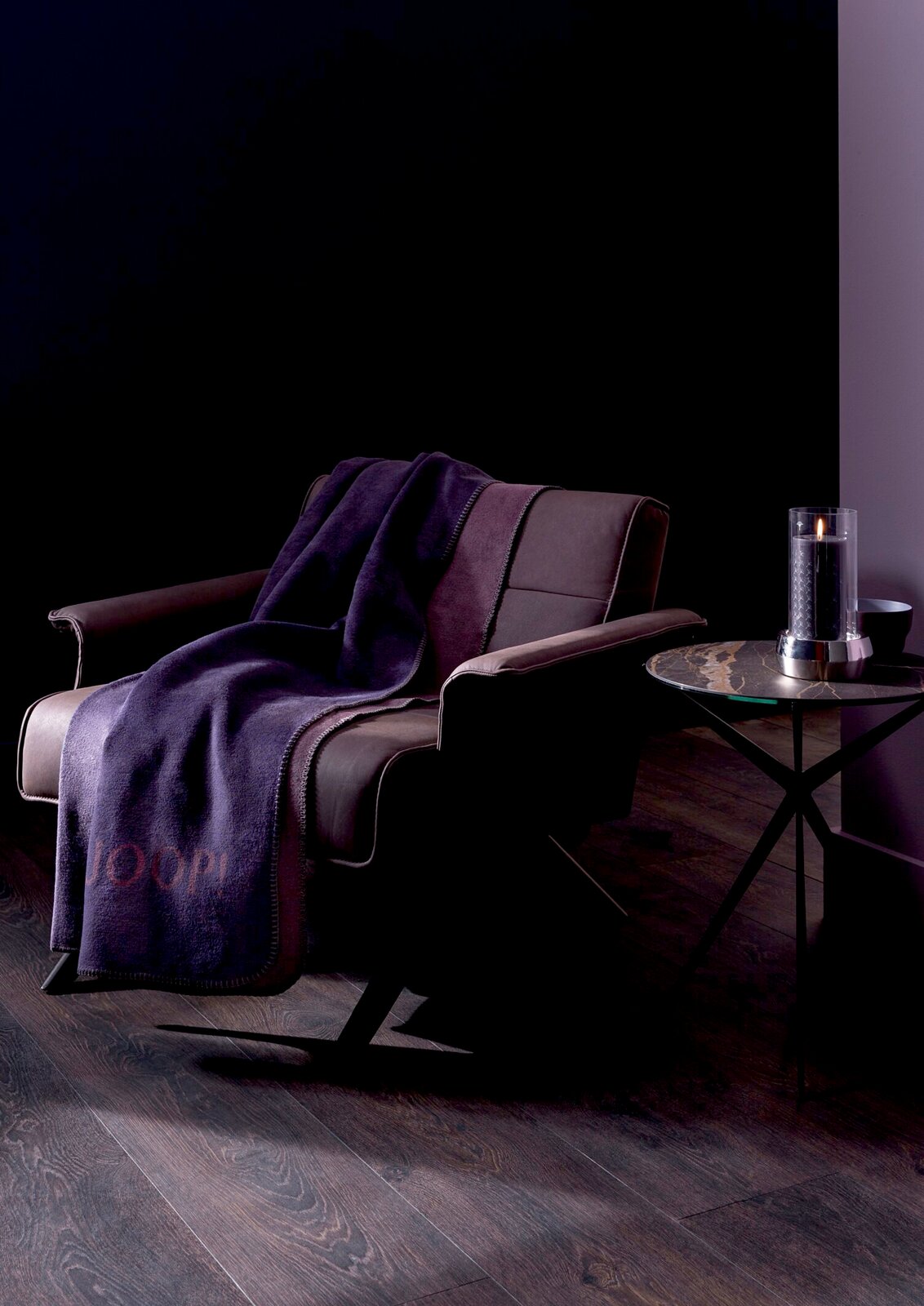 Lila Decke auf einem modernen Sessel in einem stilvollen Raum, seitliche Perspektive