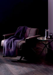 Lila Decke auf einem modernen Sessel in einem stilvollen Raum, seitliche Perspektive