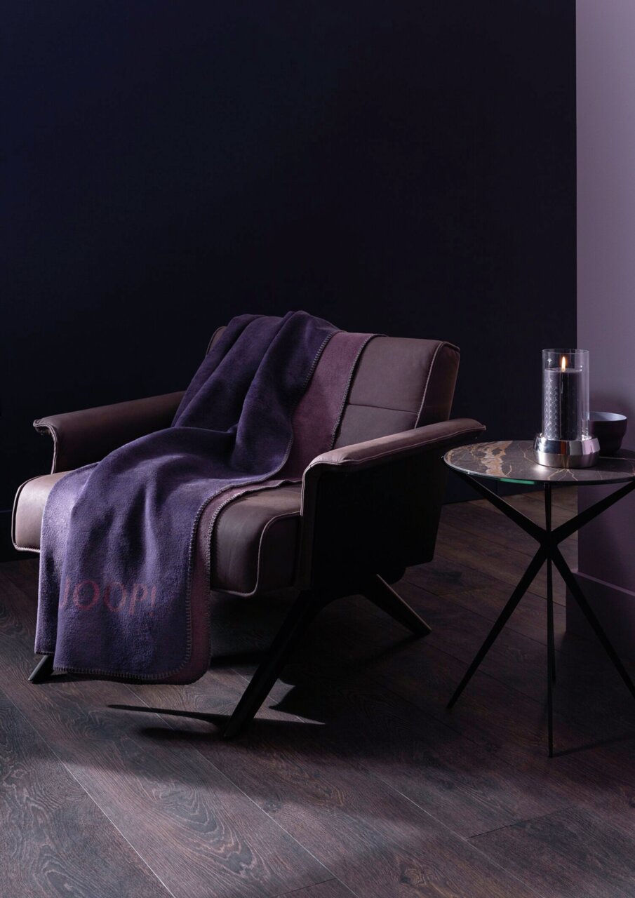 Paarse deken op een moderne fauteuil in een stijlvolle kamer, zijaanzicht