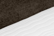 Close-up vanuit schuin bovenaanzicht van een witte matras met subtiel gewatteerd golfpatroon tegen een donkerbruine, gestructureerde bedachterwand.
