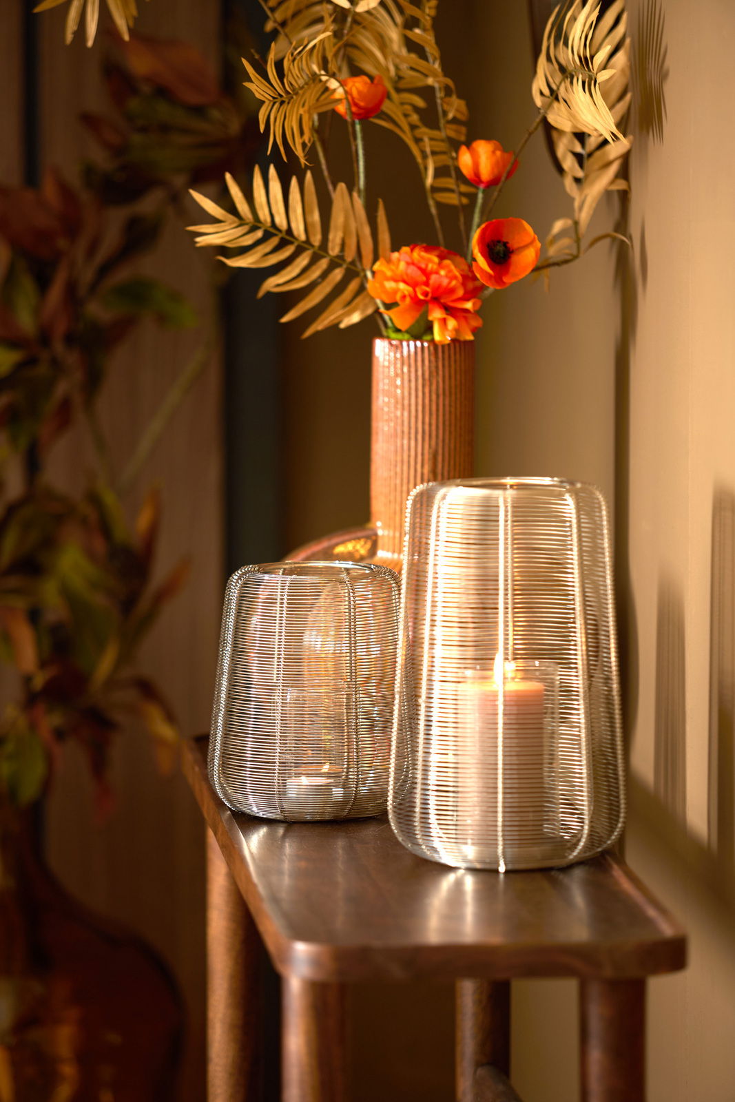 Light&Living Windlicht ADETA Zwei Windlichter aus Drahtgeflecht auf einem Holztisch, im Hintergrund eine Vase mit orangefarbenen Blumen, seitliche Perspektive.