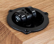 Nahaufnahme eines schwarzen Rollenmechanismus in einem Holztisch, von oben betrachtet.