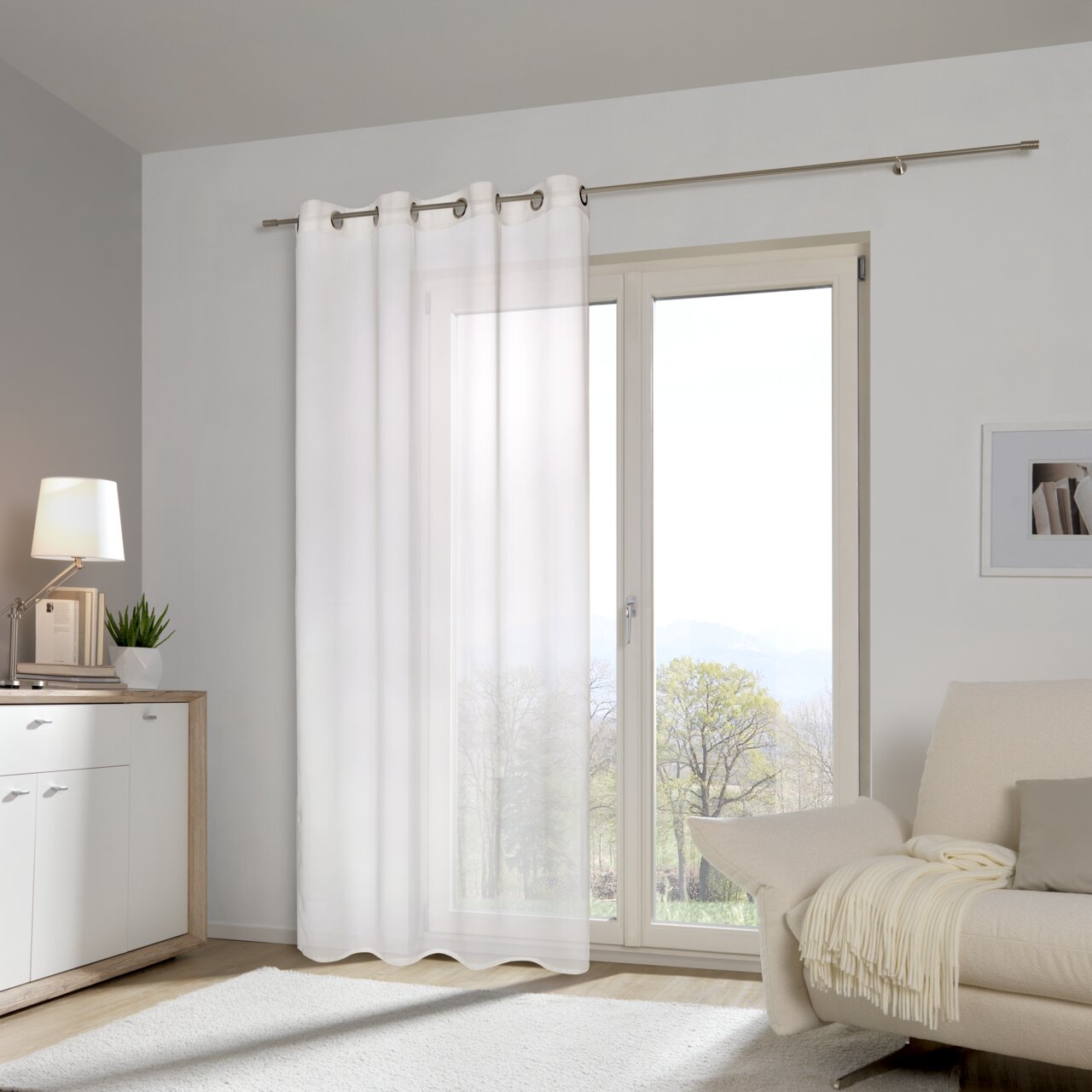 Weißer Ösenschal vor einem großen Fenster in einem modernen Wohnzimmer, seitliche Perspektive