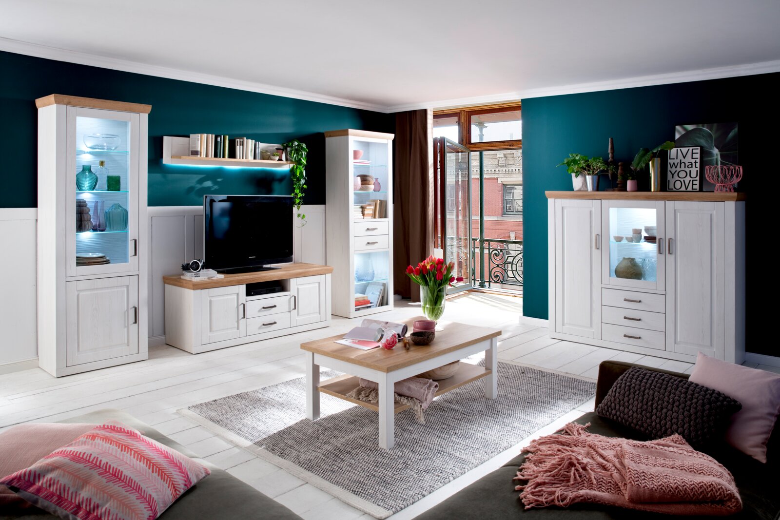 Landscape Highboard BREGENZ Helles Wohnzimmer mit weißer Wohnwand und Vitrinen mit Holzoberflächen, TV-Board, Couchtisch und Sideboard vor petrolfarbenen Wänden; perspektivische Gesamtansicht aus leicht schräger Frontansicht