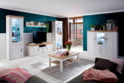 Helles Wohnzimmer mit weißer Wohnwand und Vitrinen mit Holzoberflächen, TV-Board, Couchtisch und Sideboard vor petrolfarbenen Wänden; perspektivische Gesamtansicht aus leicht schräger Frontansicht