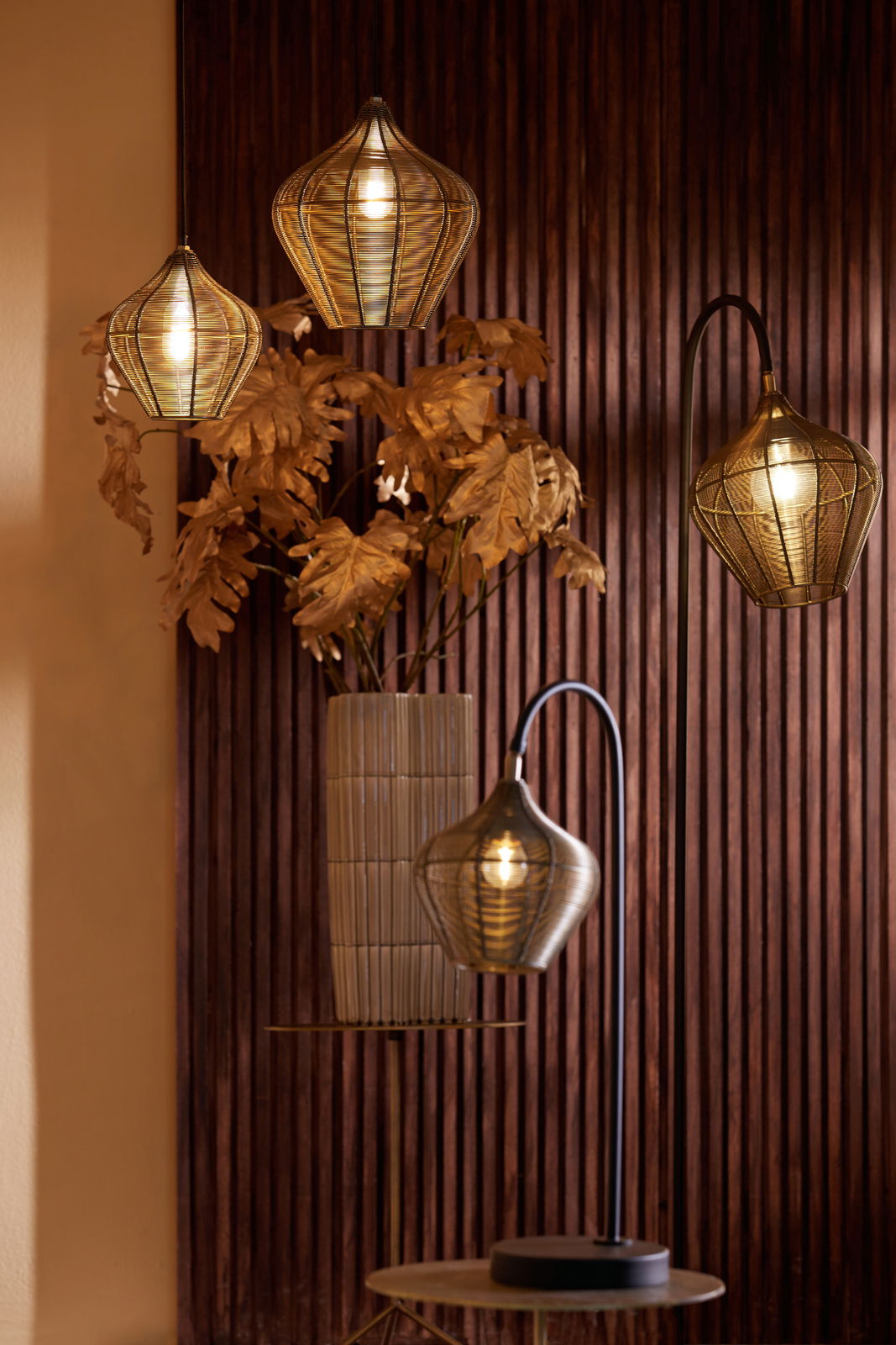 Vier Hängeleuchten in verschiedenen Höhen vor einer Holzvertäfelung, mit warmem Licht und dekorativen Blättern im Hintergrund. Perspektive von vorne.