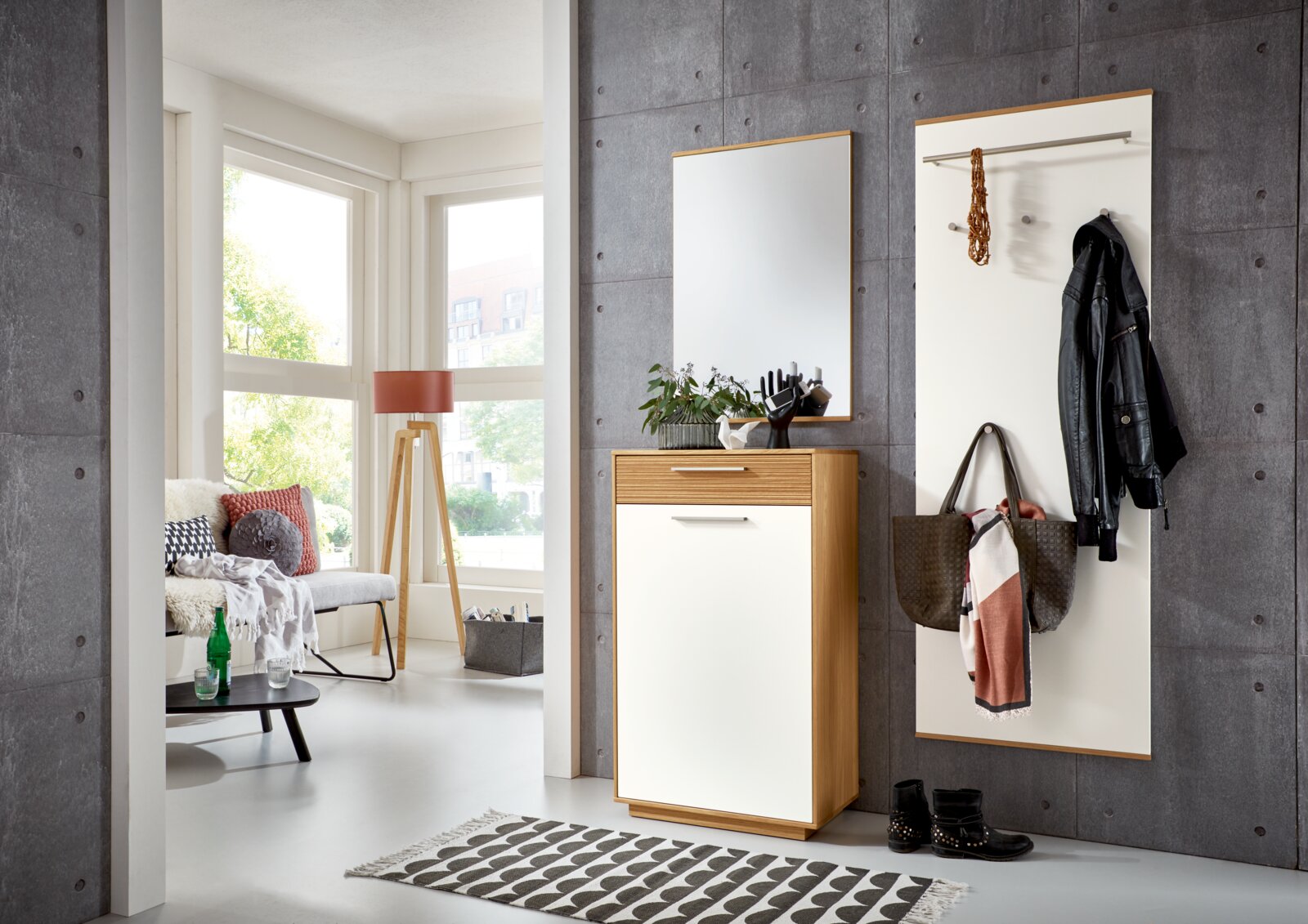 Moderne halmeubelset in de gang: smalle schoenen-/opbergkast in licht hout met witte fronten en lade, met grote wandspiegel erboven en wit kapstokpaneel met roede en haken; gefotografeerd in frontaal licht schuin zijaanzicht.