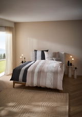 Bett mit gestreifter Bettwäsche in einem modernen Schlafzimmer, seitliche Perspektive