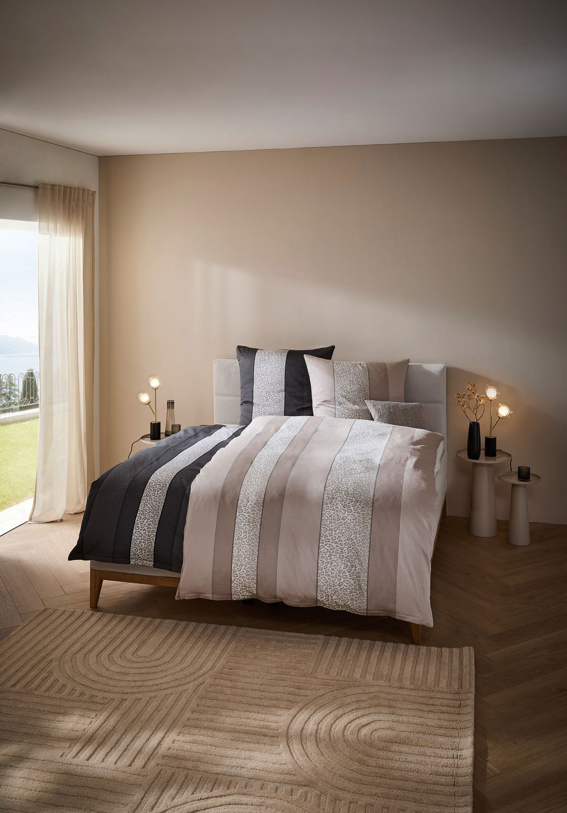 Bett mit gestreifter Bettwäsche in einem modernen Schlafzimmer, seitliche Perspektive