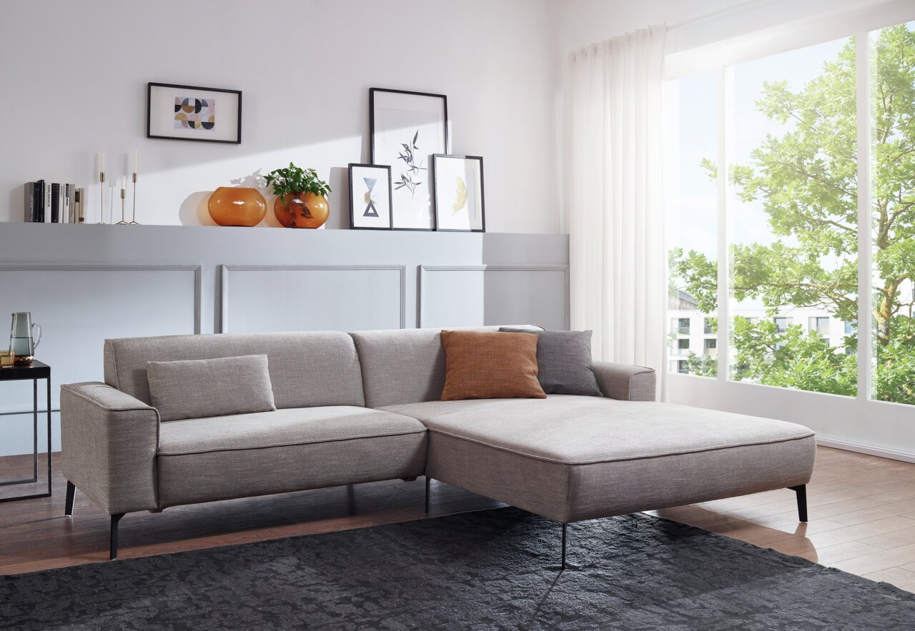 Graue Longchairkombination in einem modernen Wohnzimmer, seitliche Perspektive mit großen Fenstern im Hintergrund.