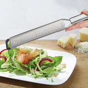 Fein- und Grobreibe PRIMELINE in der Hand gehalten, über einem Teller mit frischem Salat und geriebenem Käse im Hintergrund, seitliche Perspektive.