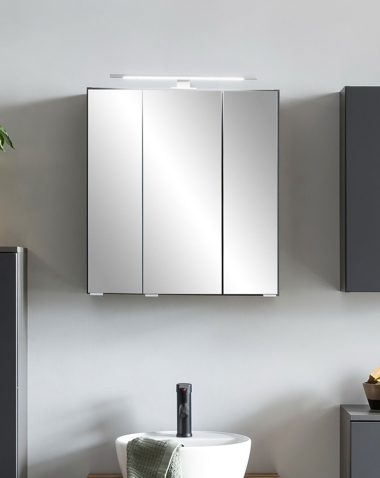 Moderner Spiegelschrank mit drei Türen und integrierter Beleuchtung, frontal betrachtet über einem Waschbecken montiert.