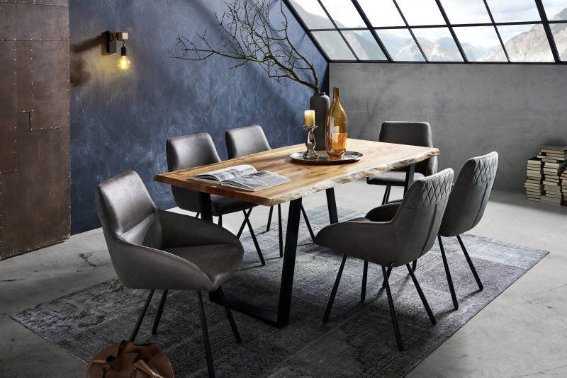 Esszimmer mit modernem Holztisch und V-Gestell, umgeben von sechs grauen Stühlen, in einem stilvollen Raum mit schrägem Fenster und Bergblick, aus seitlicher Perspektive.