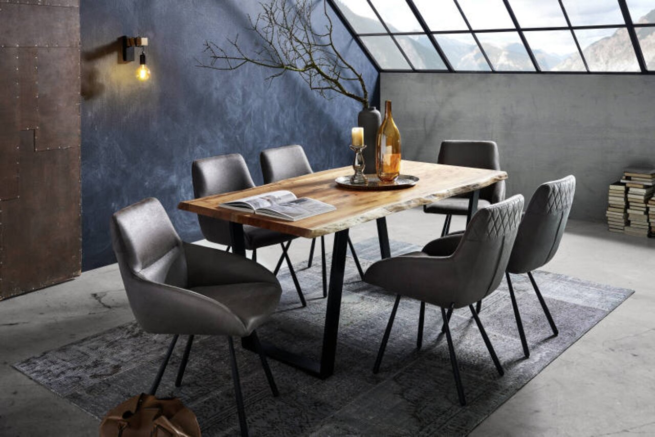 Esszimmer mit modernem Holztisch und V-Gestell, umgeben von sechs grauen Stühlen, in einem stilvollen Raum mit schrägem Fenster und Bergblick, aus seitlicher Perspektive.