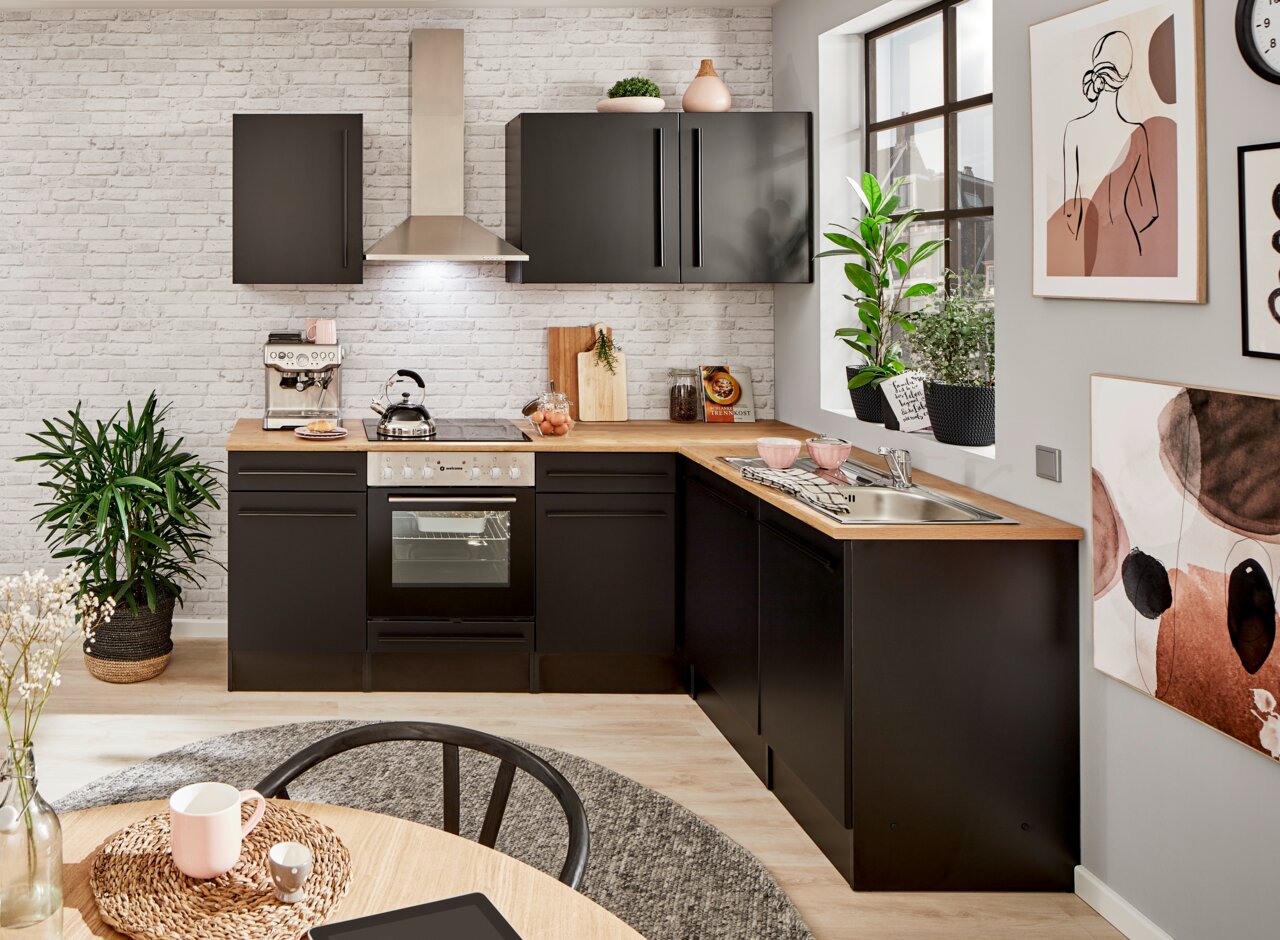 Moderne Küche mit schwarzem Eckunterschrank, Holzarbeitsplatte und Edelstahlspüle, aus der Perspektive von vorne rechts betrachtet.