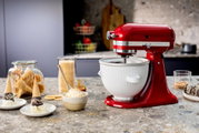 Rote Küchenmaschine Liebesapfel auf einer Küchenarbeitsplatte, umgeben von Eiswaffeln und Dessertschalen, seitliche Perspektive.
