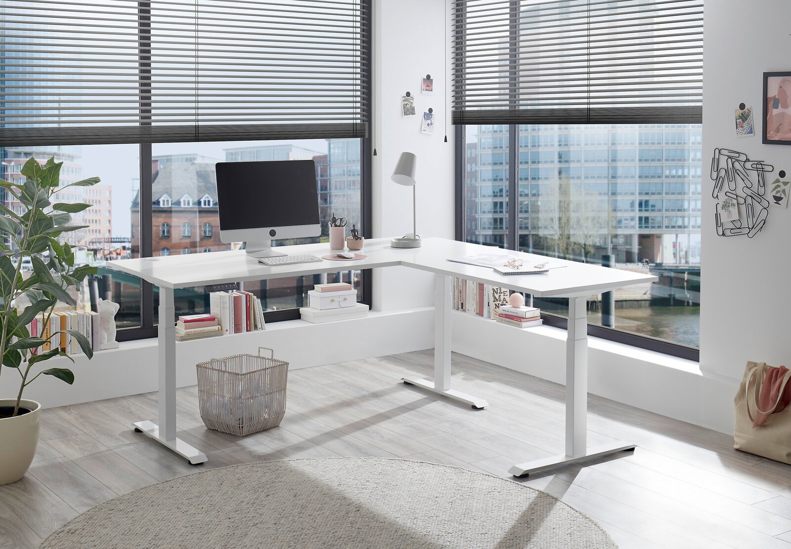 Moderner weißer E-Eckschreibtisch in einem hellen Büro mit großen Fenstern, seitliche Perspektive.