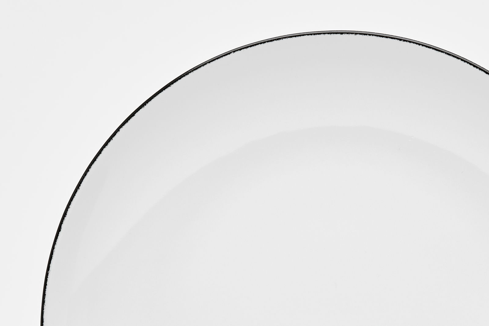 Nahaufnahme eines weißen Tellers mit schwarzem Rand, von oben betrachtet.