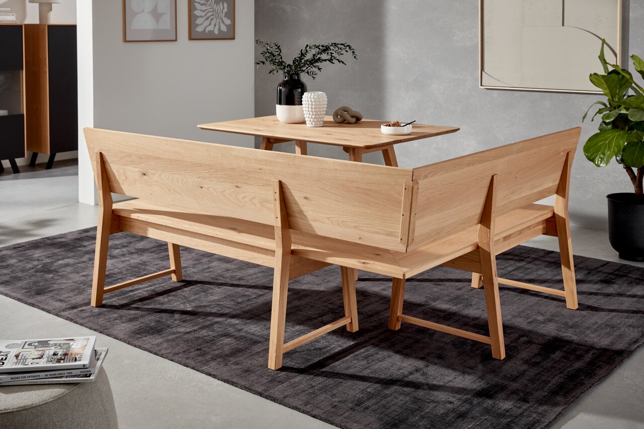 Achterkant van een houten hoekbank in een moderne woonkamer, met een tafel en decoraties.