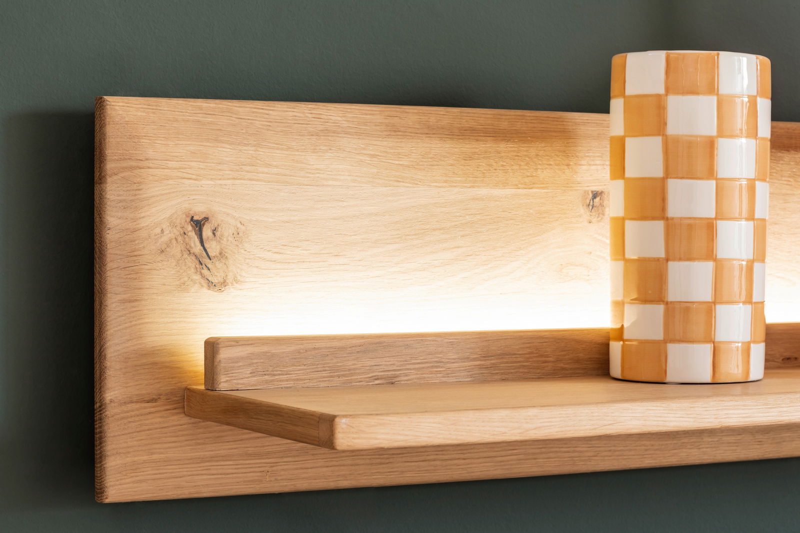 Nahaufnahme einer Wandkombination aus Holz mit integrierter Beleuchtung und einer dekorativen Vase in Schachbrettmuster.