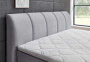 Seitliche Ansicht eines grauen Boxspringbetts mit gepolstertem Kopfteil und strukturierter Matratze in einem modernen Schlafzimmer.