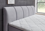 Seitliche Ansicht eines grauen Boxspringbetts mit gepolstertem Kopfteil und strukturierter Matratze in einem modernen Schlafzimmer.