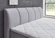 Seitliche Ansicht eines grauen Boxspringbetts mit gepolstertem Kopfteil und strukturierter Matratze in einem modernen Schlafzimmer.