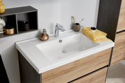Modernes Badezimmer-Waschbecken in Weiß auf Waschtischunterschrank in Holzoptik mit Chromarmatur, Seifenspender und gelbem Handtuch, aufgenommen aus schräger Vorderansicht leicht von oben.