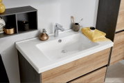 Modernes Badezimmer-Waschbecken in Weiß auf Waschtischunterschrank in Holzoptik mit Chromarmatur, Seifenspender und gelbem Handtuch, aufgenommen aus schräger Vorderansicht leicht von oben.