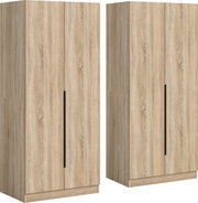 Zweitüriger Kleiderschrank in heller Holzoptik mit langen schwarzen Griffleisten, freistehend auf Sockel, in schräger Frontansicht (3/4-Perspektive) vor weißem Hintergrund