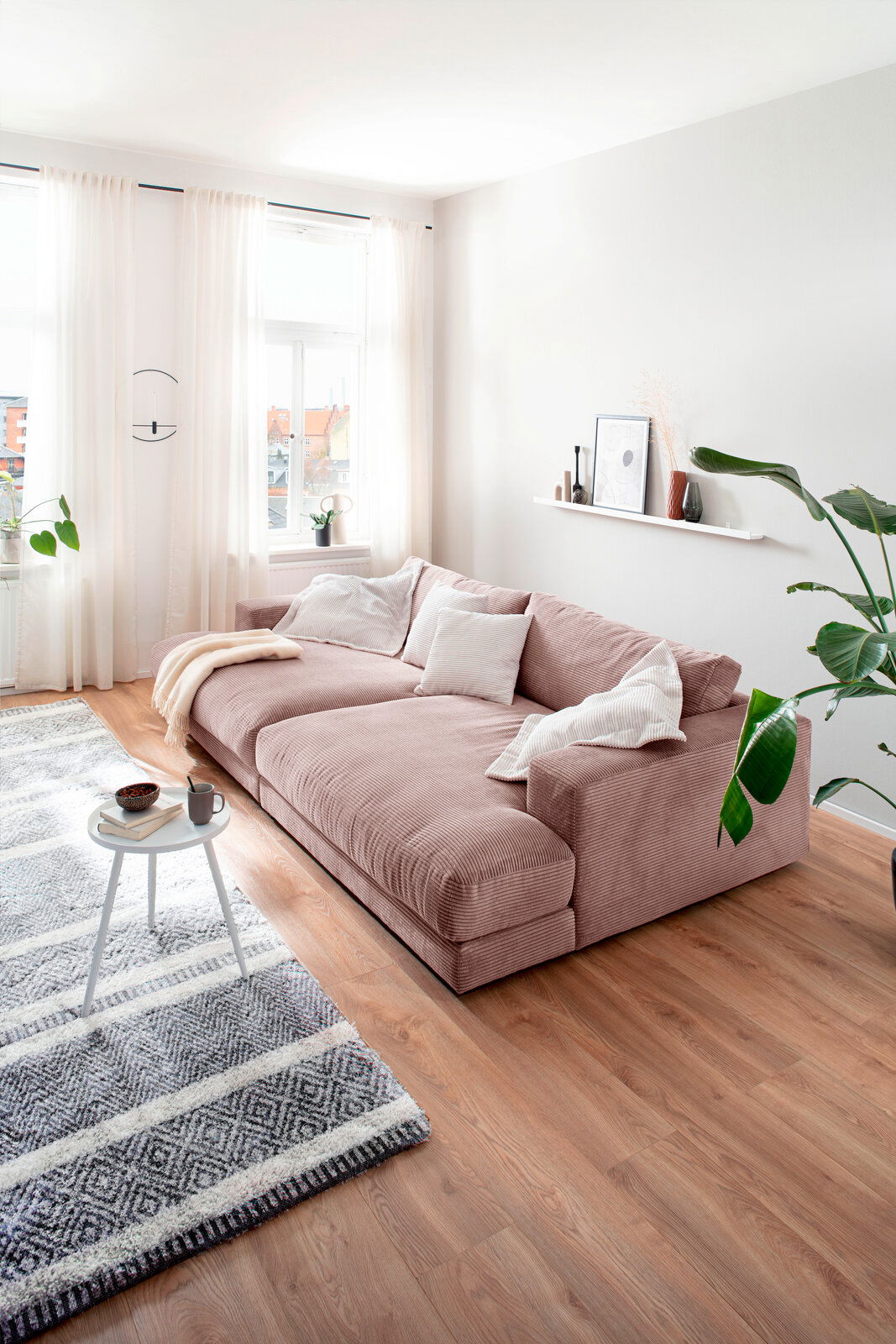 Großes Megasofa in einem hellen Wohnzimmer, seitliche Perspektive, mit weichen Kissen und einer Decke dekoriert.