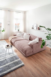 Großes Megasofa in einem hellen Wohnzimmer, seitliche Perspektive, mit weichen Kissen und einer Decke dekoriert.