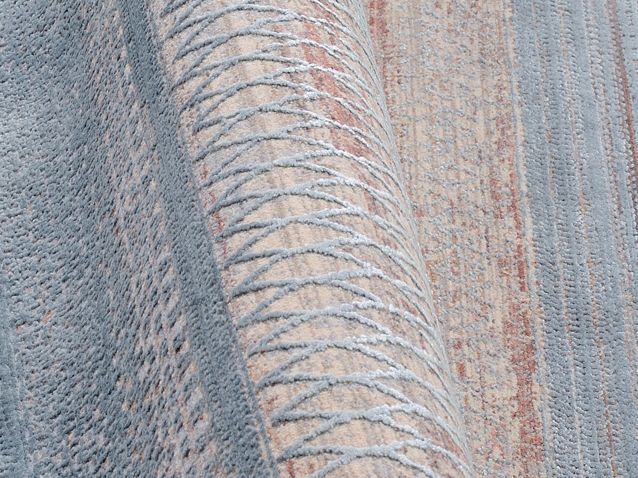 Nahaufnahme eines Designer-Teppichs mit geometrischem Muster in Blau- und Beigetönen, seitliche Perspektive