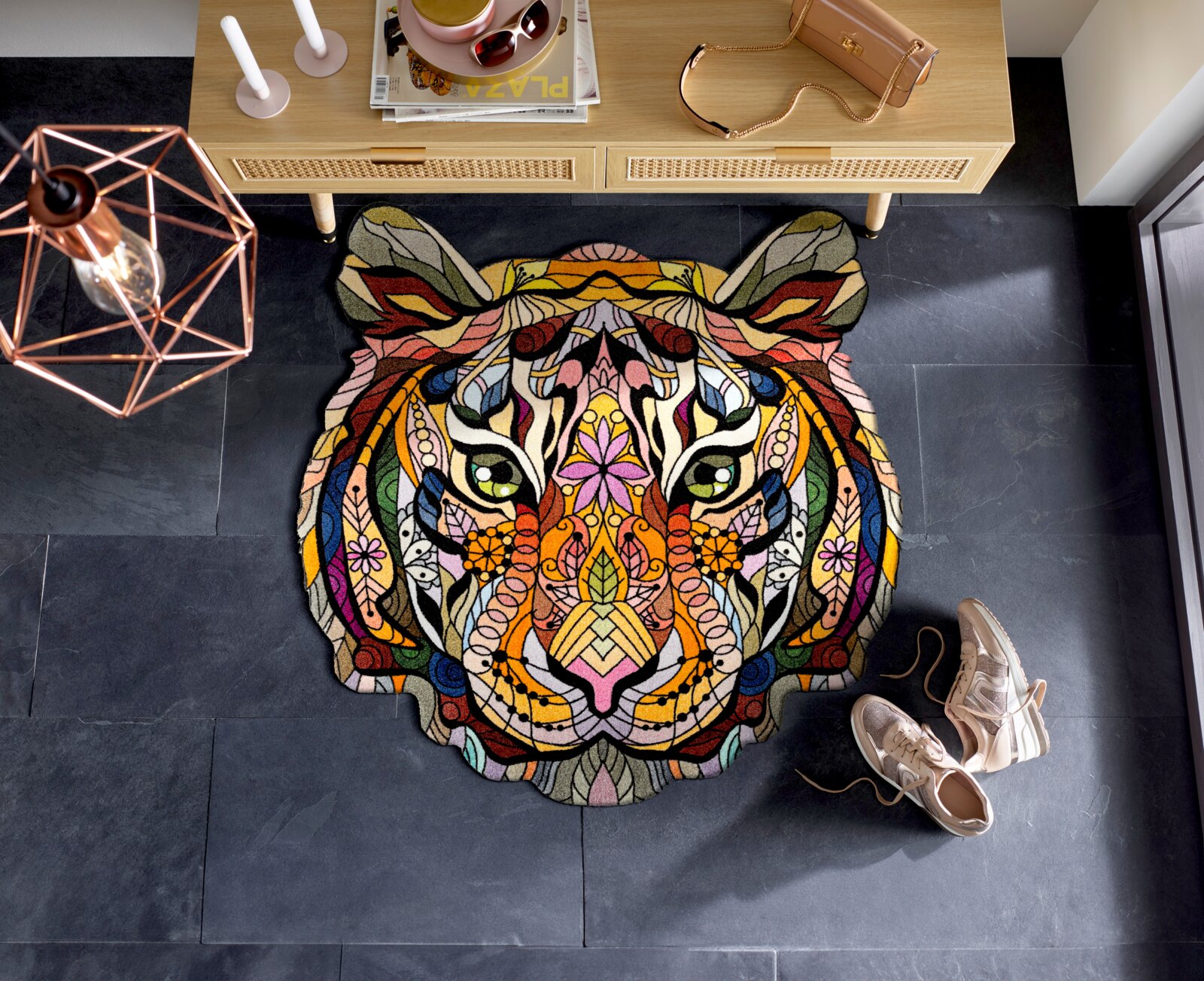 Bunte, kunstvolle Tigerkopf-Matte auf dunklem Boden, von oben betrachtet, mit dekorativen Elementen und Schuhen daneben.