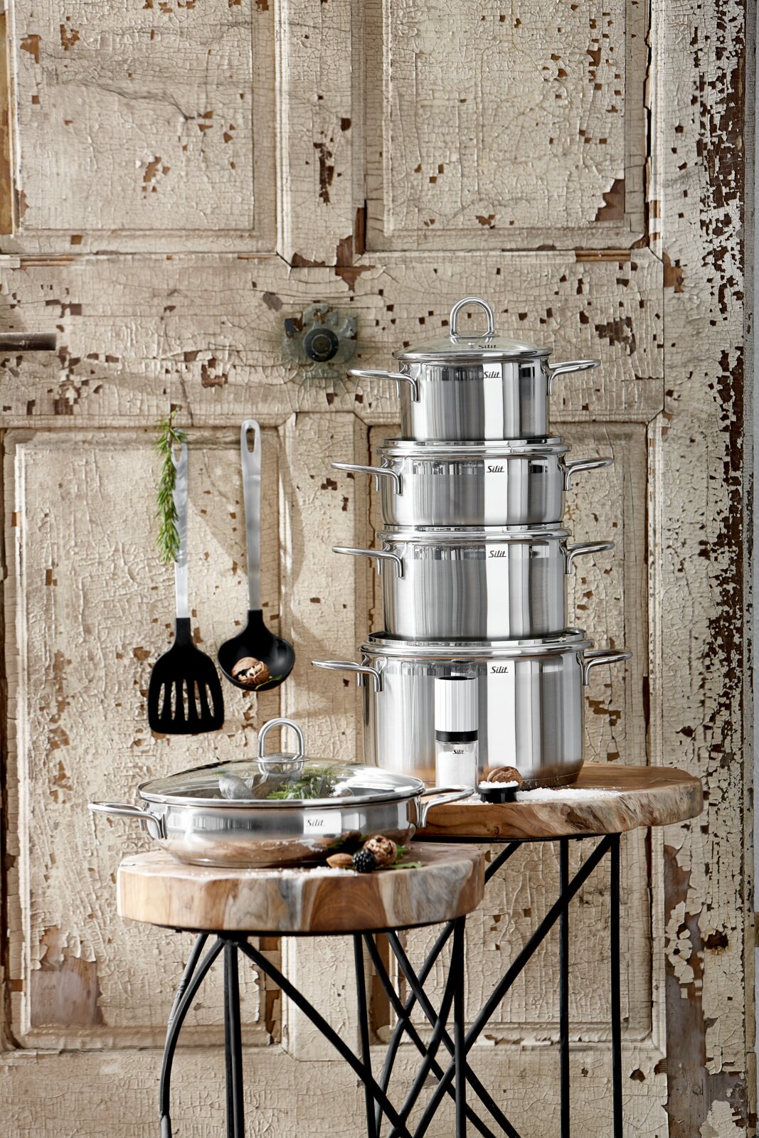 Stapel von glänzenden Edelstahltöpfen auf rustikalem Holztisch vor antiker Holzwand, seitliche Perspektive