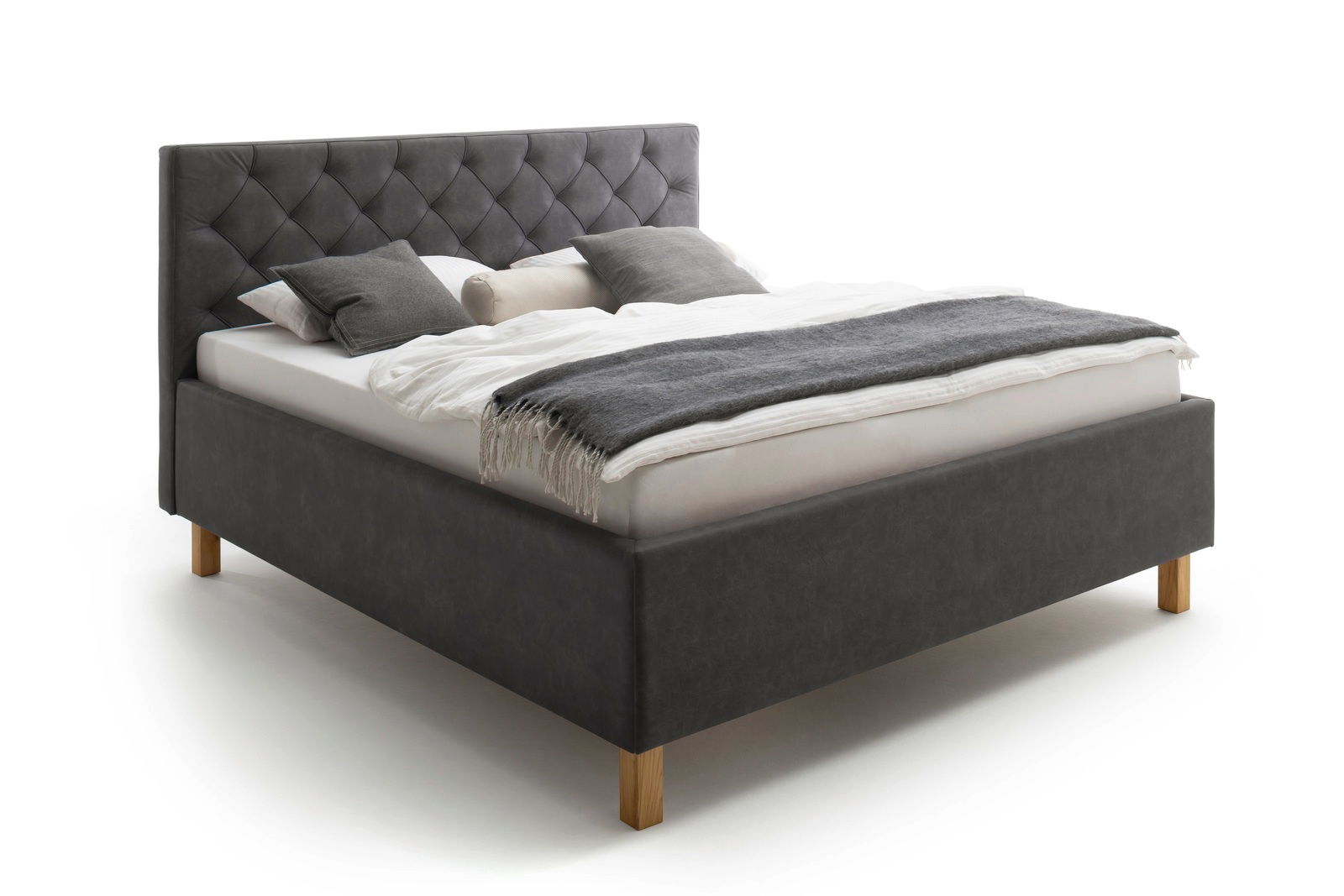 Polsterbett in seitlicher Perspektive mit grauem Kopfteil und Holzfüßen, dekoriert mit Kissen und Decke.