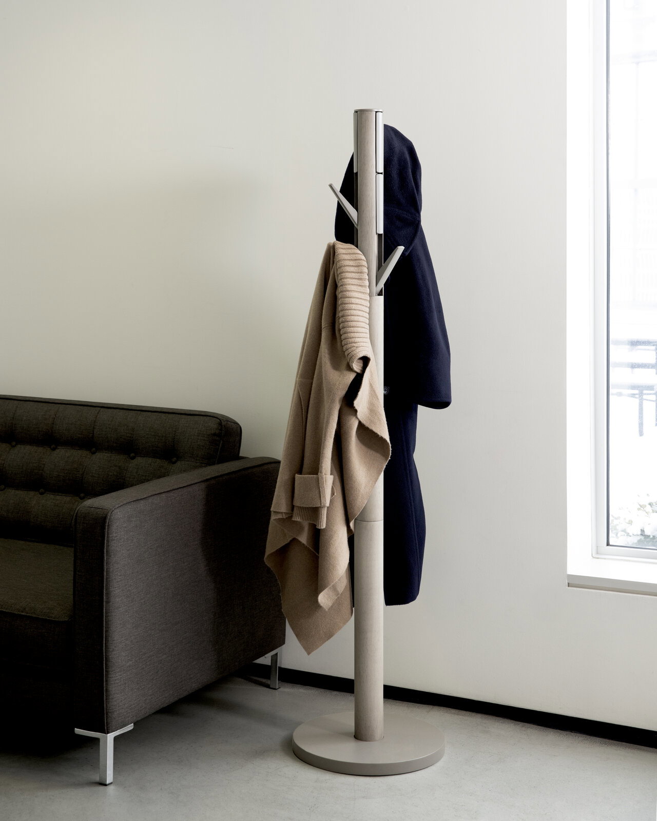 Moderner Garderobenständer aus Metall mit mehreren Haken, fotografiert aus seitlicher Perspektive neben einem Sofa und einem Fenster.