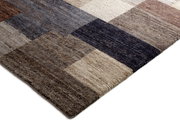 Nahaufnahme eines Wollteppichs mit einem geometrischen Muster in verschiedenen Brauntönen, von der Seite fotografiert.