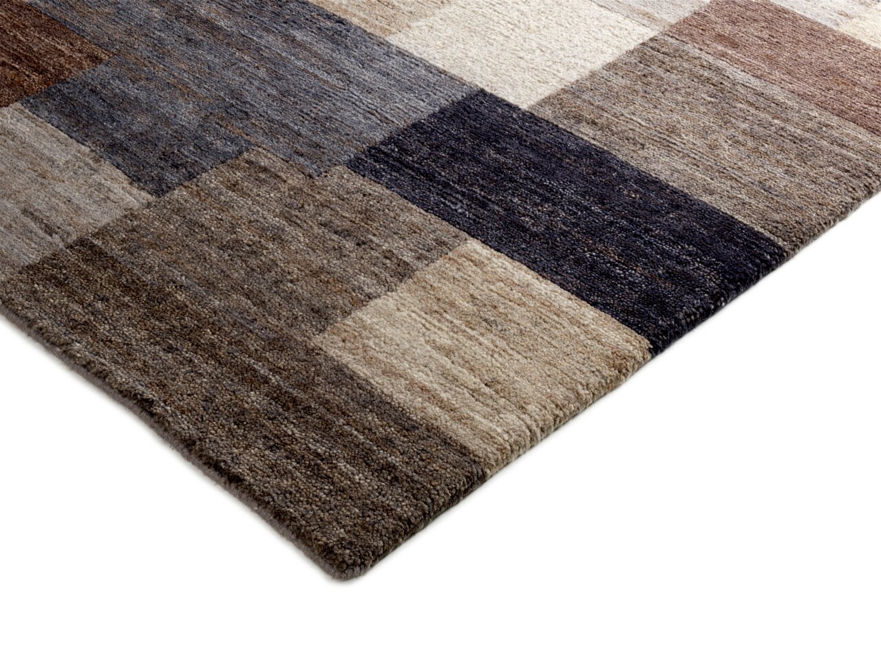 Nahaufnahme eines Wollteppichs mit einem geometrischen Muster in verschiedenen Brauntönen, von der Seite fotografiert.